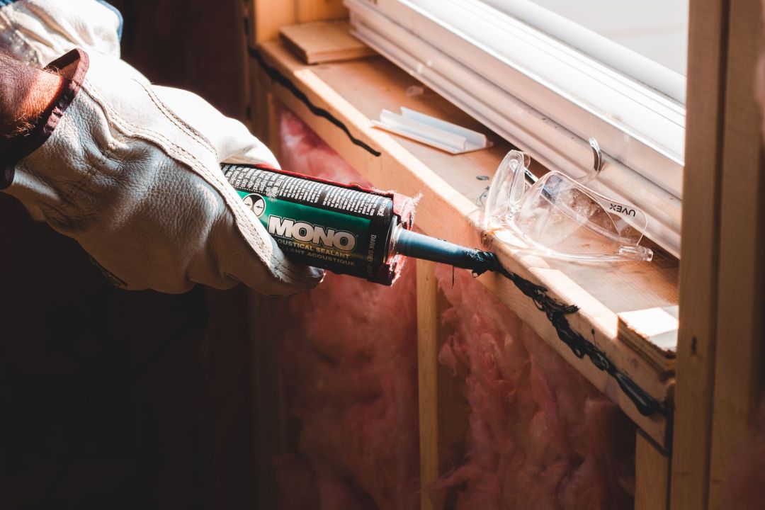 Handwerker zieht mit der Kartusche eine Dichtfuge am Anschluss eines Fensterrahmens.